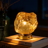 Amber cast glass rock lamp glowing on a gold disc base on a stack of books
