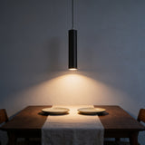 Black LED cylinder pendant light hanging low over a walnut dining table