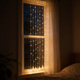 LED curtain string lights hanging down a bedroom window at night