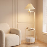 Cream floor lamp with pleated shade and built-in round side table beside a boucle armchair