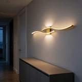 Gold wave-shaped LED wall bar glowing above a sideboard in a hallway