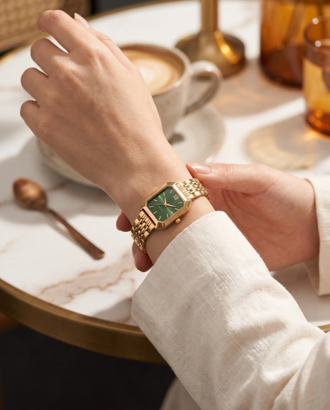 Gold quartz watch with green dial worn at a cafe table
