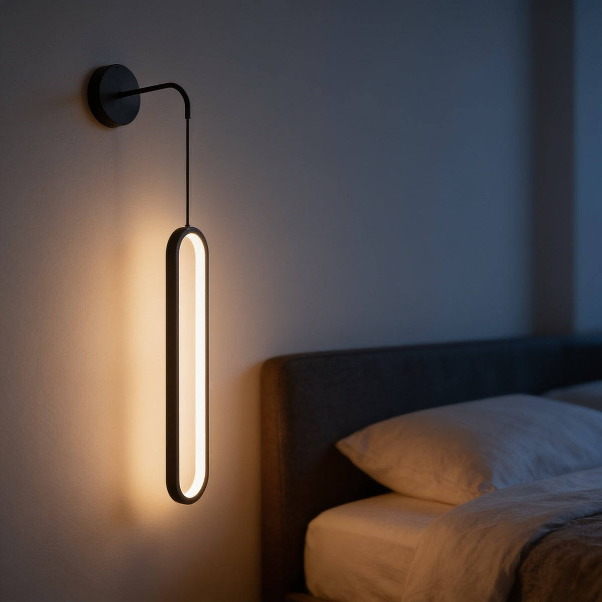 Black bedside wall sconce with a hanging oval LED beside a bed