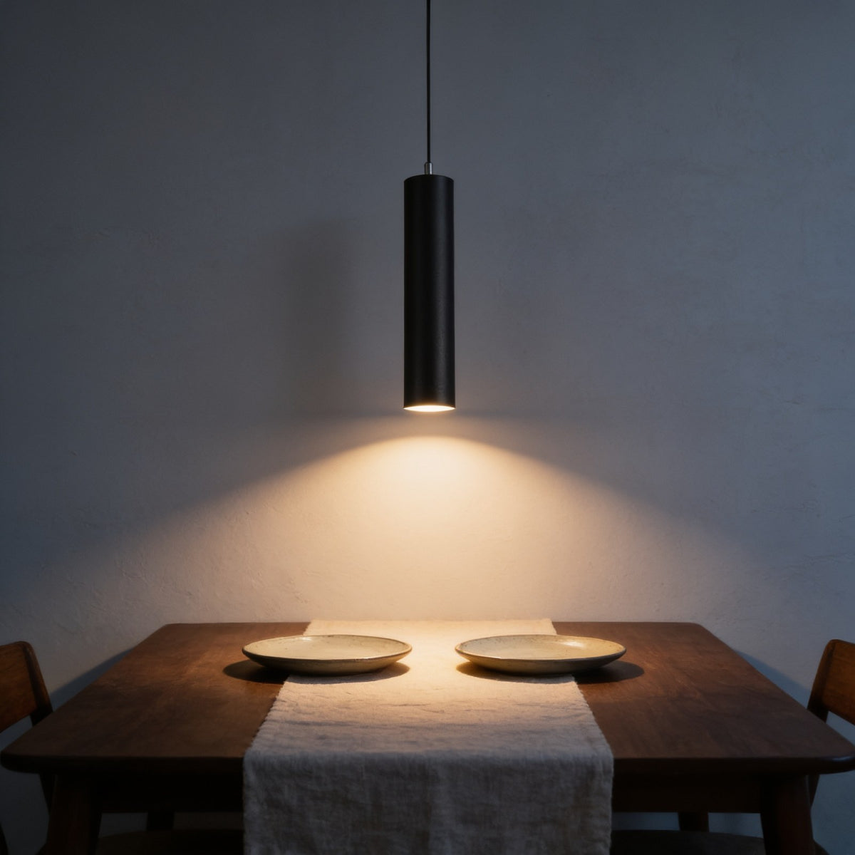 Black LED cylinder pendant light hanging low over a walnut dining table
