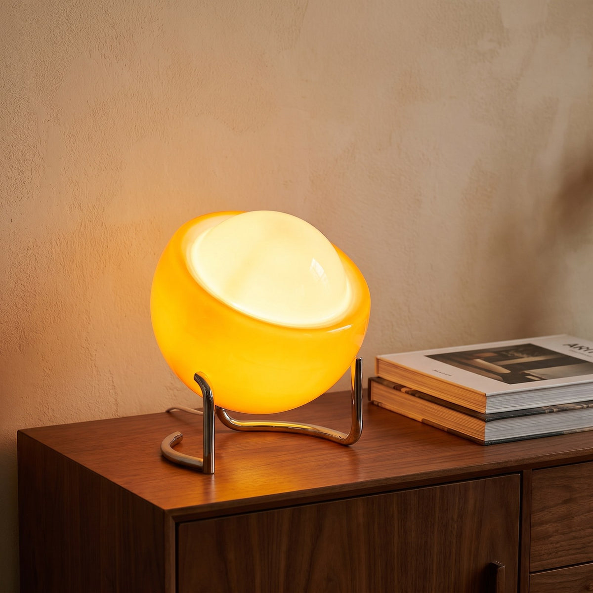 Handmade amber glass globe table lamp on a chrome cradle glowing on a walnut sideboard