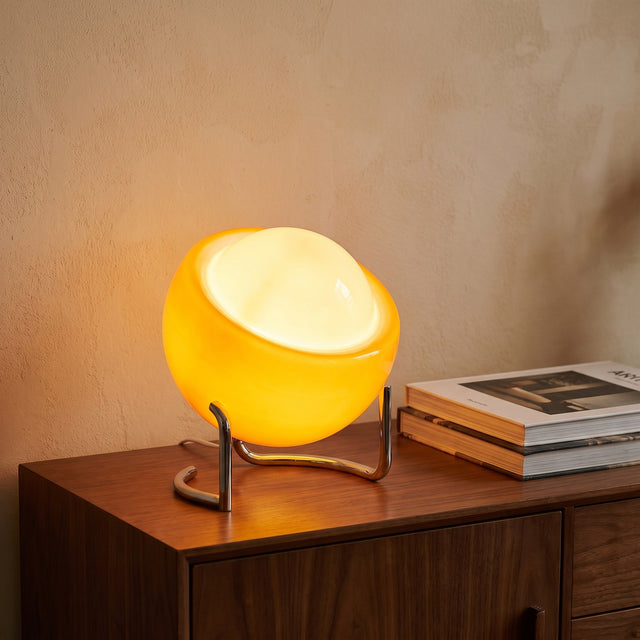 Handmade amber glass globe table lamp on a chrome cradle glowing on a walnut sideboard