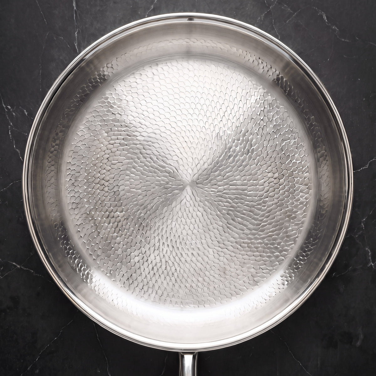 Overhead view of the titanium frying pan on a black marble counter, showing the hammered fish-scale cooking surface