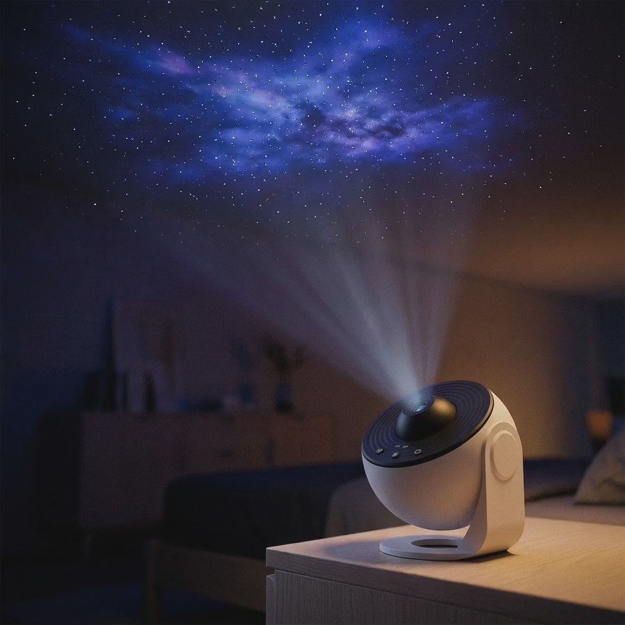 The galaxy projector on a nightstand, projecting a drifting starfield and nebula across a dark bedroom ceiling