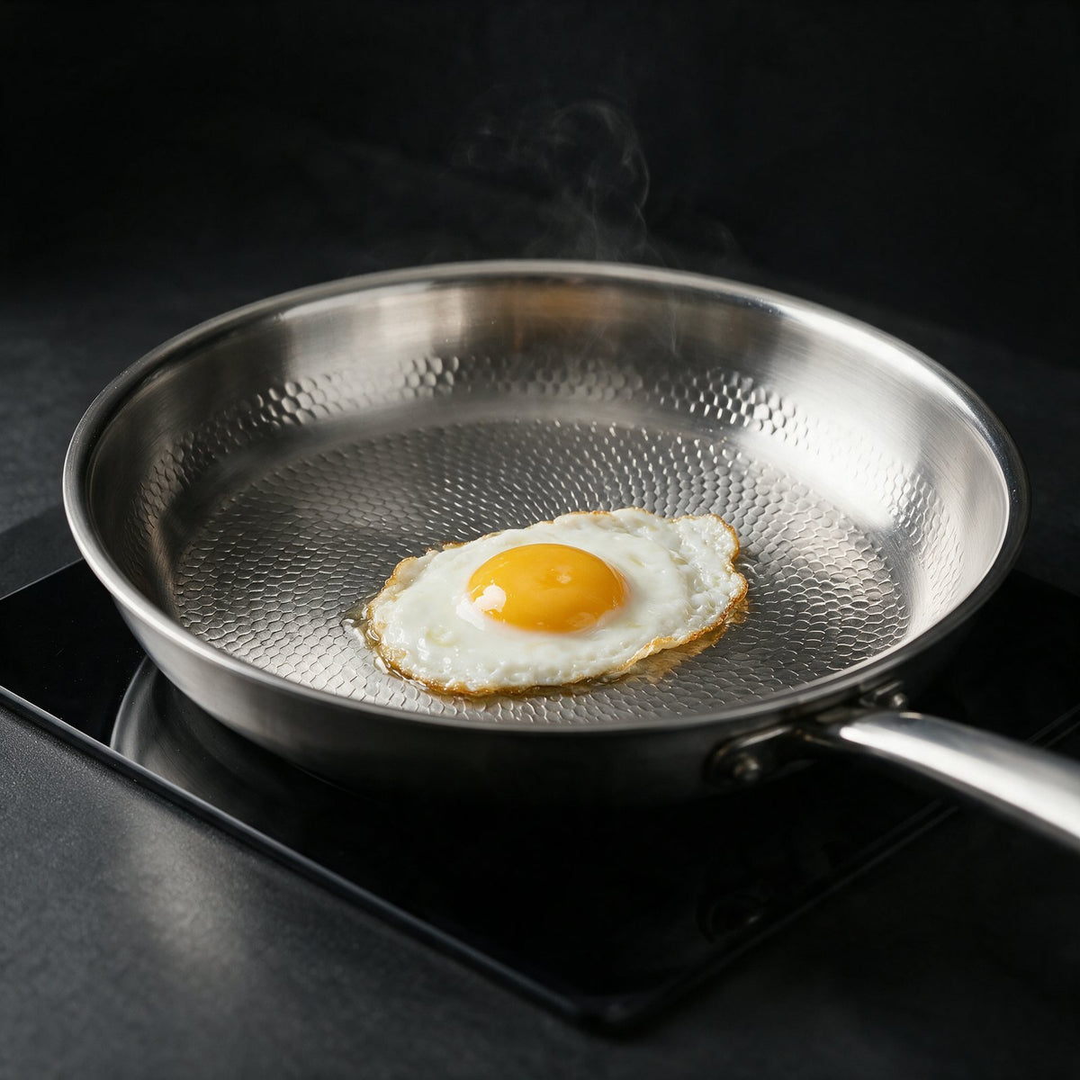 A fried egg sliding freely across the bare hammered titanium surface of the pan on a black induction hob