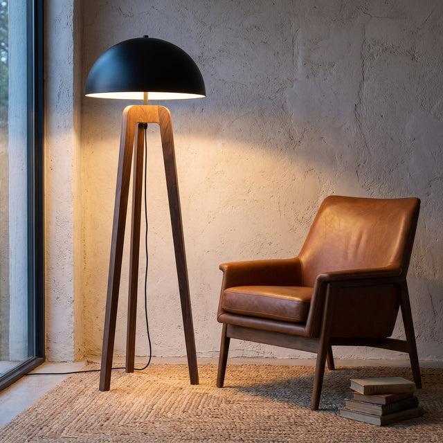 Solid walnut tripod floor lamp with black dome shade beside a leather lounge chair